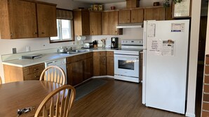 Una cucina compatta con mobili in legno, un frigorifero bianco, forno integrato e un tavolo con sedie.