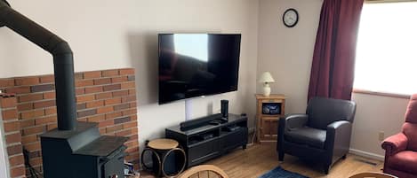 A living room with a brick fireplace, a TV, a wooden table, and a red chair.