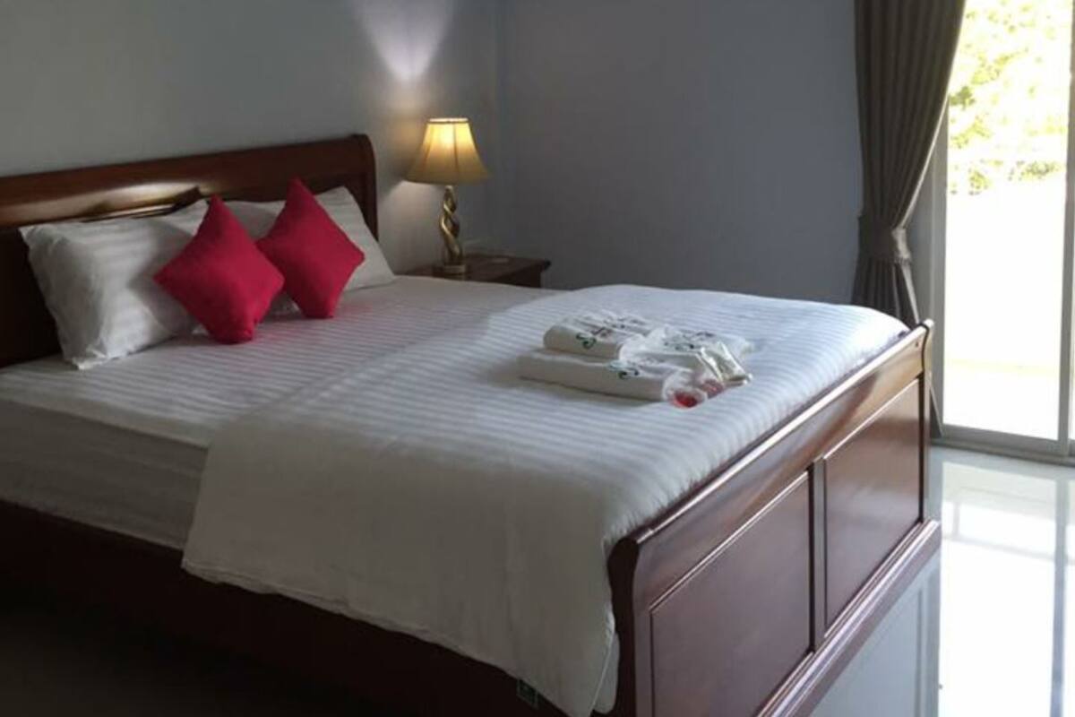 A neatly made bed with white and red pillows, a bedside lamp, and a window with curtains.