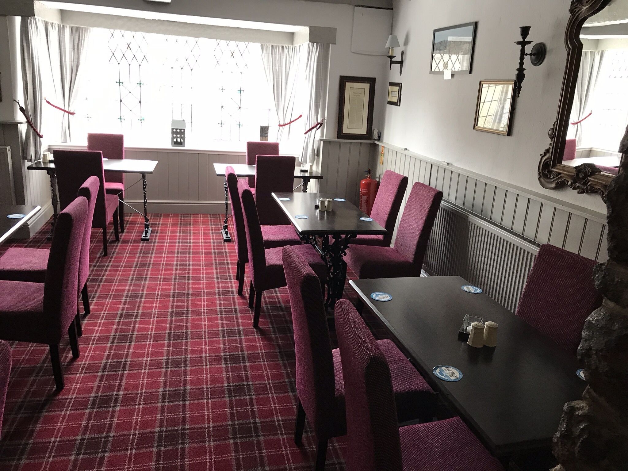 A dining area with red plaid flooring, red upholstered chairs, and a black table. There are framed pictures on the wall and a large mirror.