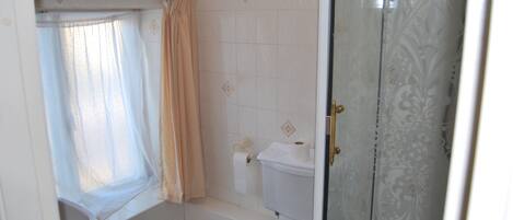 Une salle de bain comprenant des toilettes, un espace douche et une fenêtre avec un rideau.
