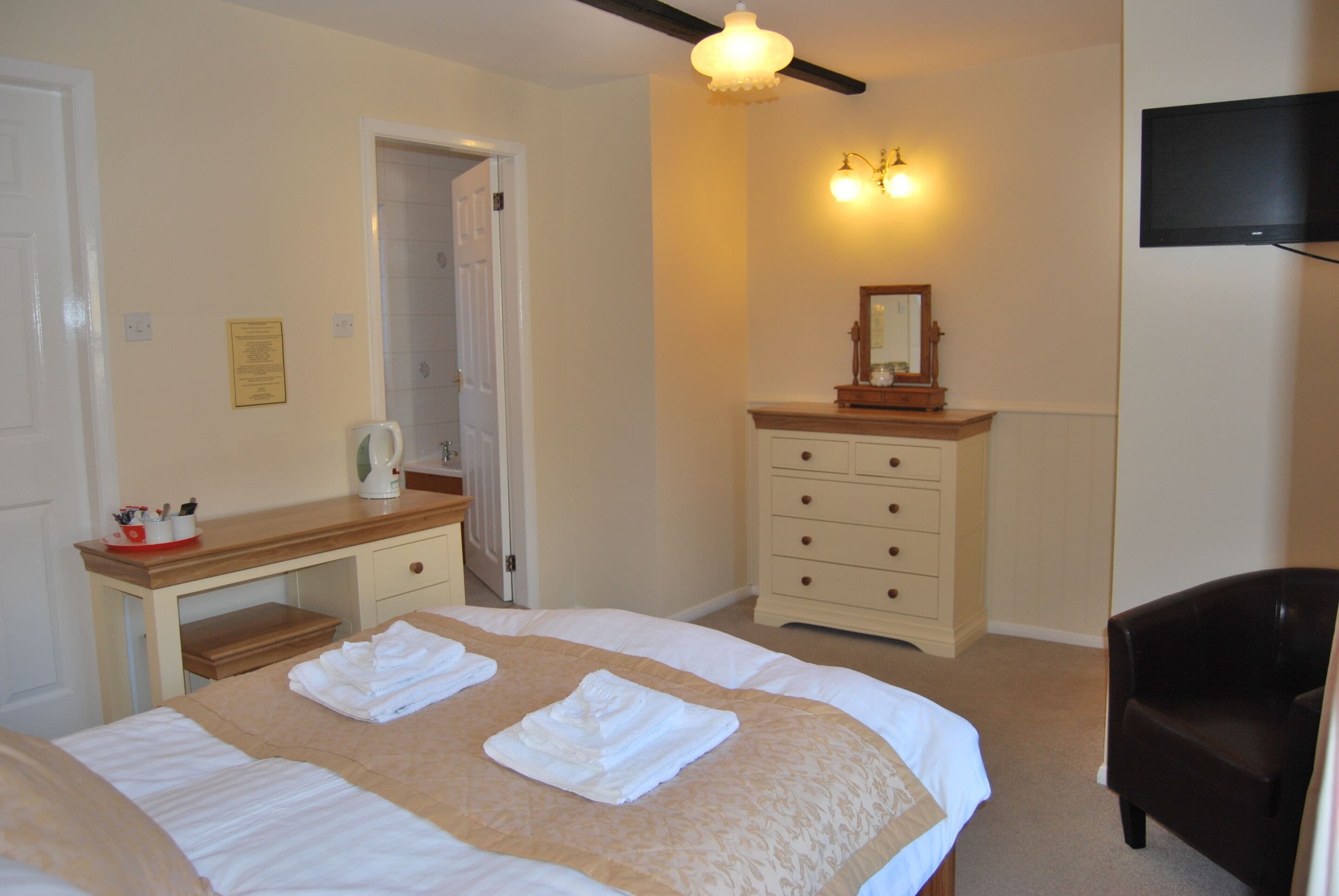 A hotel room with a bed, a dresser, a mirror, a television, and a door leading to another room.