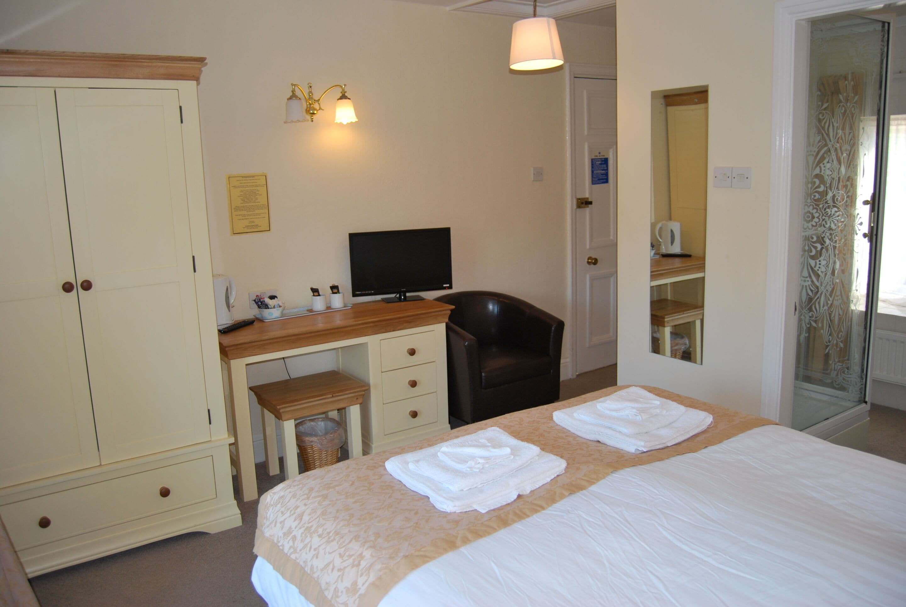 A hotel room with a bed, a desk, a chair, a television, and a wardrobe.