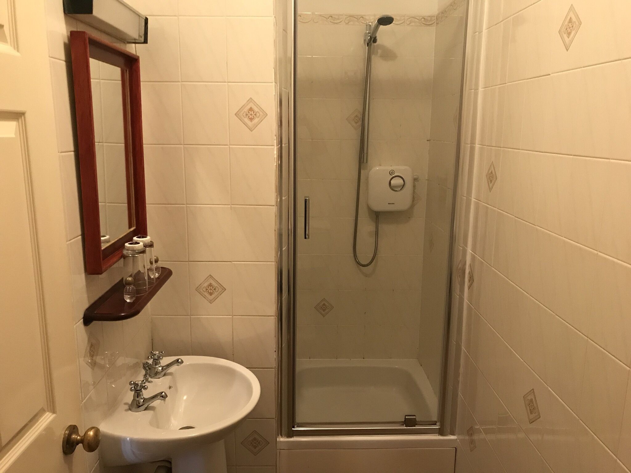 A bathroom with a glass-enclosed shower, a white sink, and a mirror with a wooden frame.