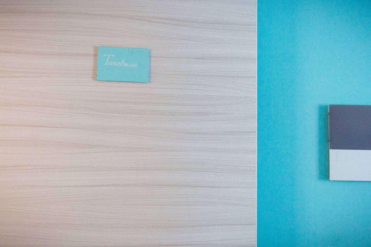 Una habitación con suelo de madera clara y una pared de acento color verde azulado. Hay una pequeña tarjeta verde azulado con la palabra "Turelese" escrita.