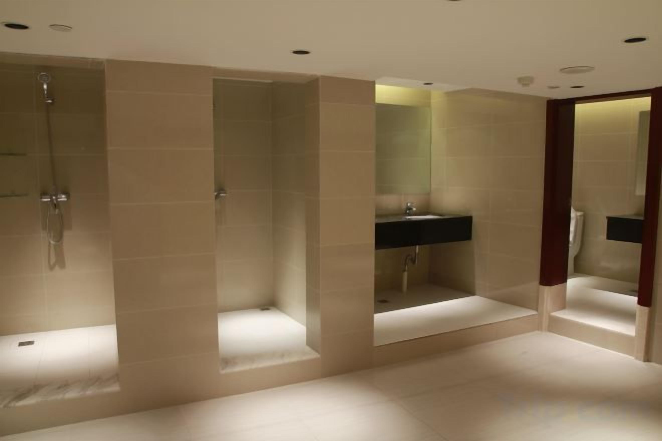 A modern bathroom with three separate shower stalls, a central sink, and a large mirror.