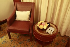 Un sillón de cuero marrón con un cojín blanco, una mesa de vidrio con frutas y una caja de pañuelos, además de una alfombra estampada.