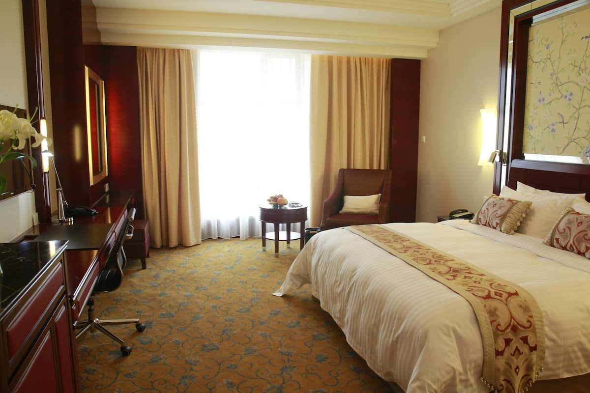 Ein Hotelzimmer mit einem großen Bett, einem Schreibtisch, einem Stuhl und einem kleinen Tisch mit einer Lampe.