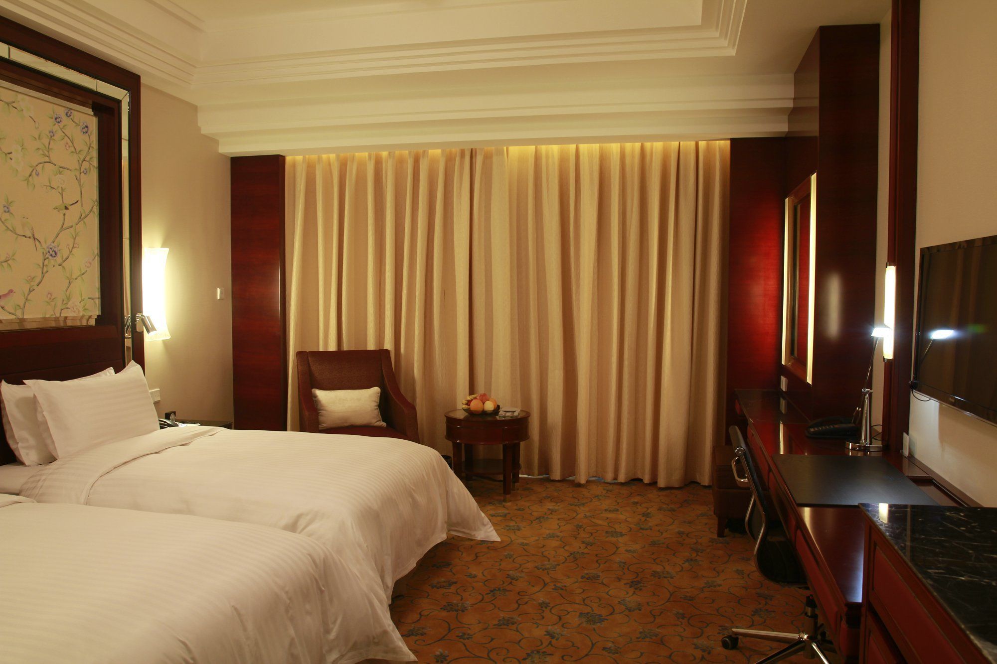 Une chambre d’hôtel avec un grand lit, un bureau avec une chaise, une télévision et un rideau.