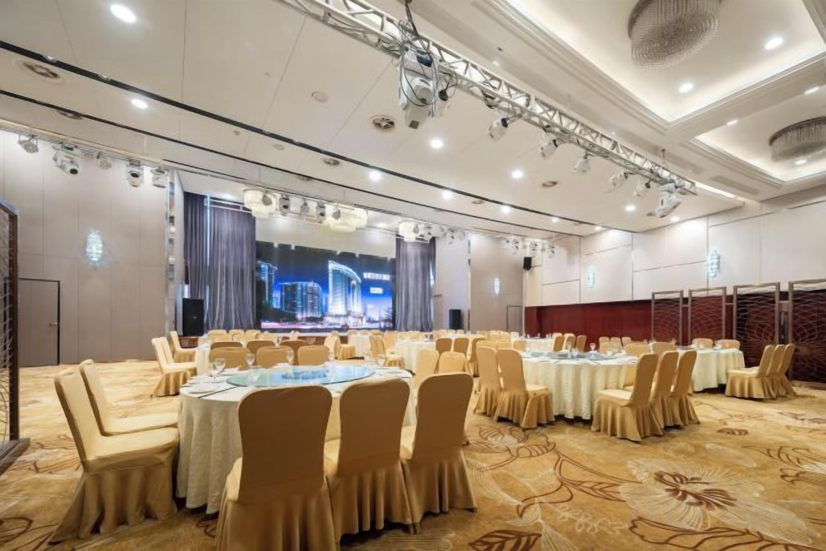 A banquet hall with round tables, chairs, and a stage.