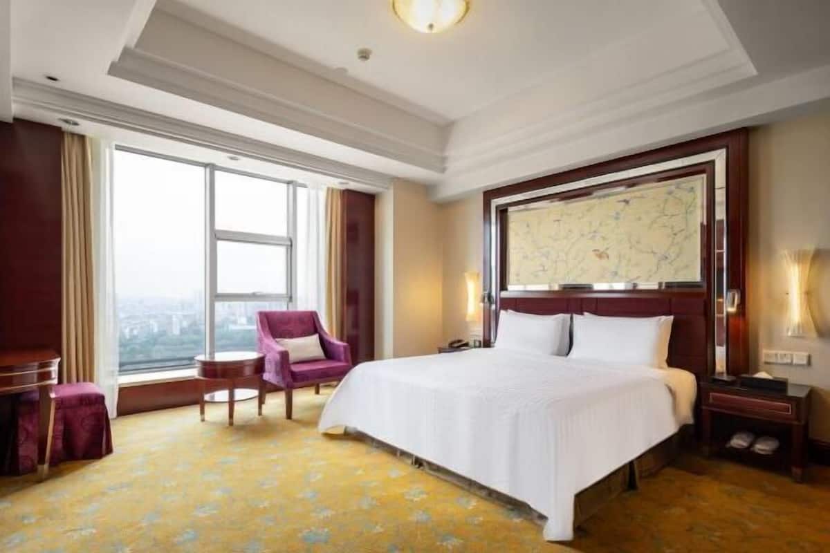Ein Hotelzimmer mit einem großen Bett, einem Sessel, einem Schreibtisch und einem Fenster mit Blick.