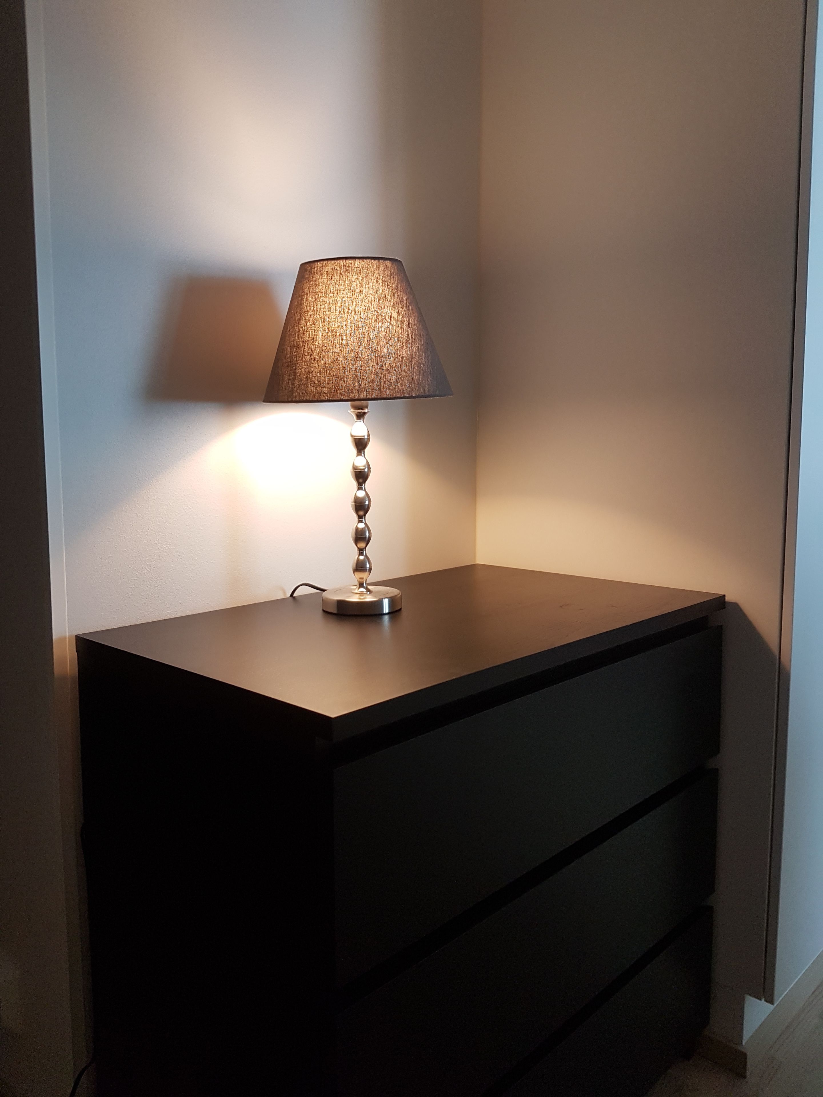 Ein Nachttisch mit Lampe, einer Schublade und einer Wand.