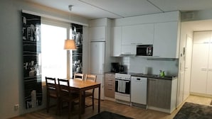 A compact kitchen with white cabinets, a microwave, a stove, and a sink. There is a dining table with chairs and a hanging light fixture.