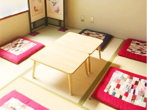 A tatami mat room with a low wooden table and four tatami mats with quilted covers. - Hostel J Culture168 (Toyonaka)