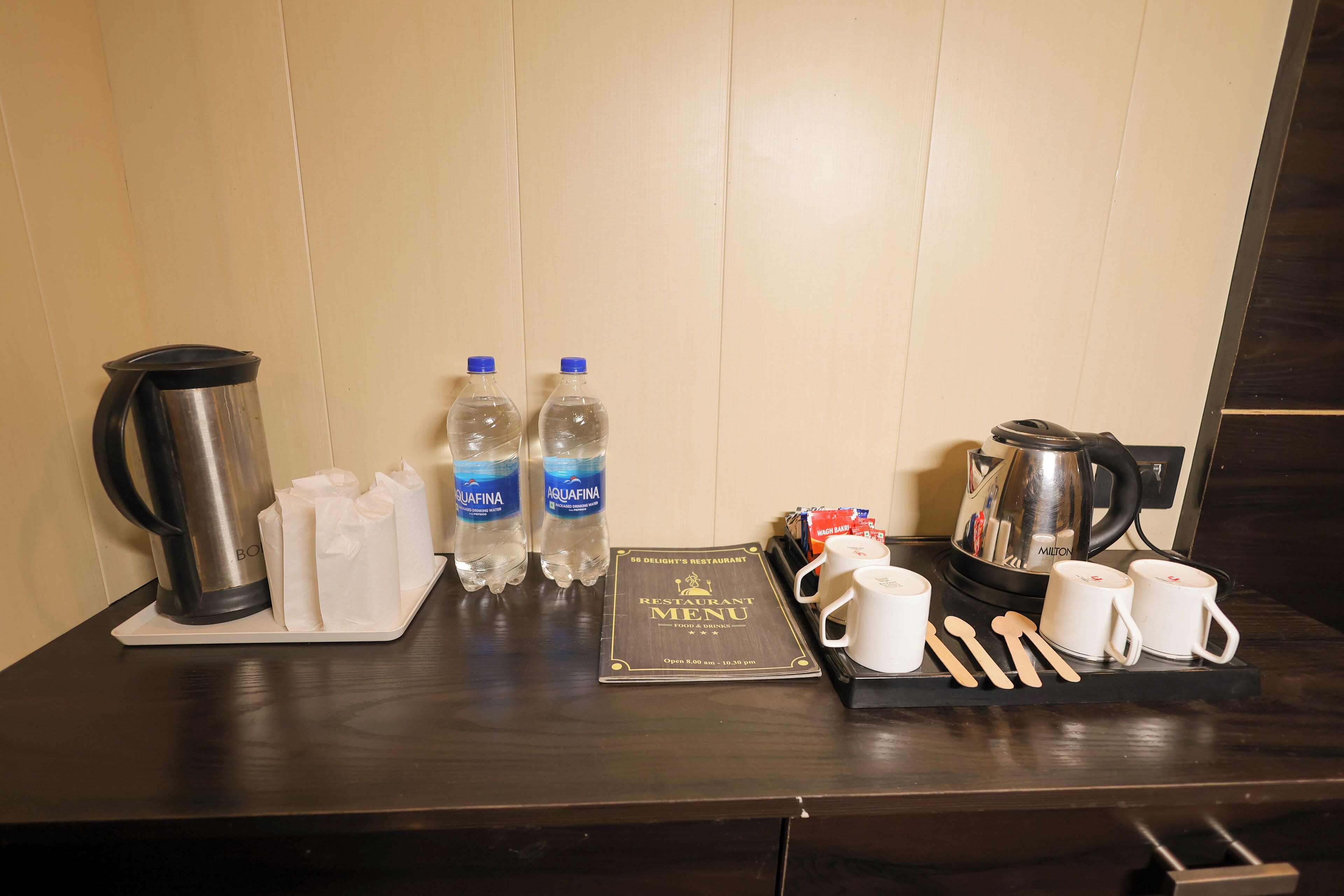 A hotel room's breakfast setup with a coffee maker, two bottles of water, a menu, and utensils.
