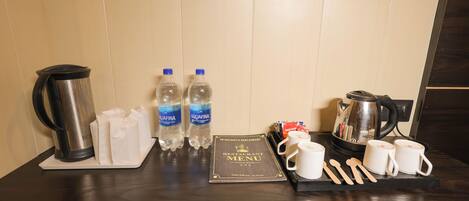 A hotel room's breakfast setup with a coffee maker, two bottles of water, a menu, and utensils.