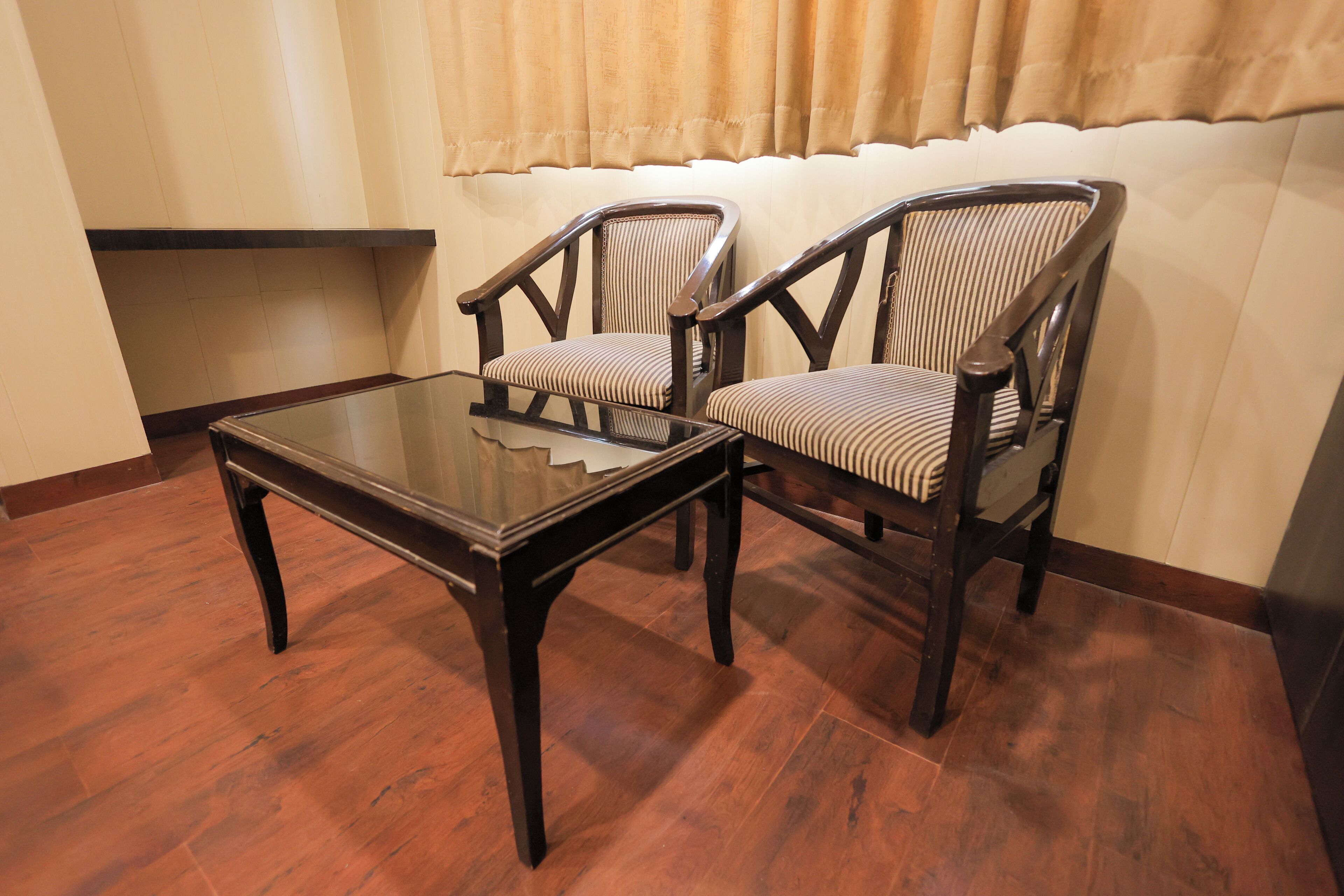 A room with two wooden chairs with striped cushions, a glass-top table, and a wooden floor.