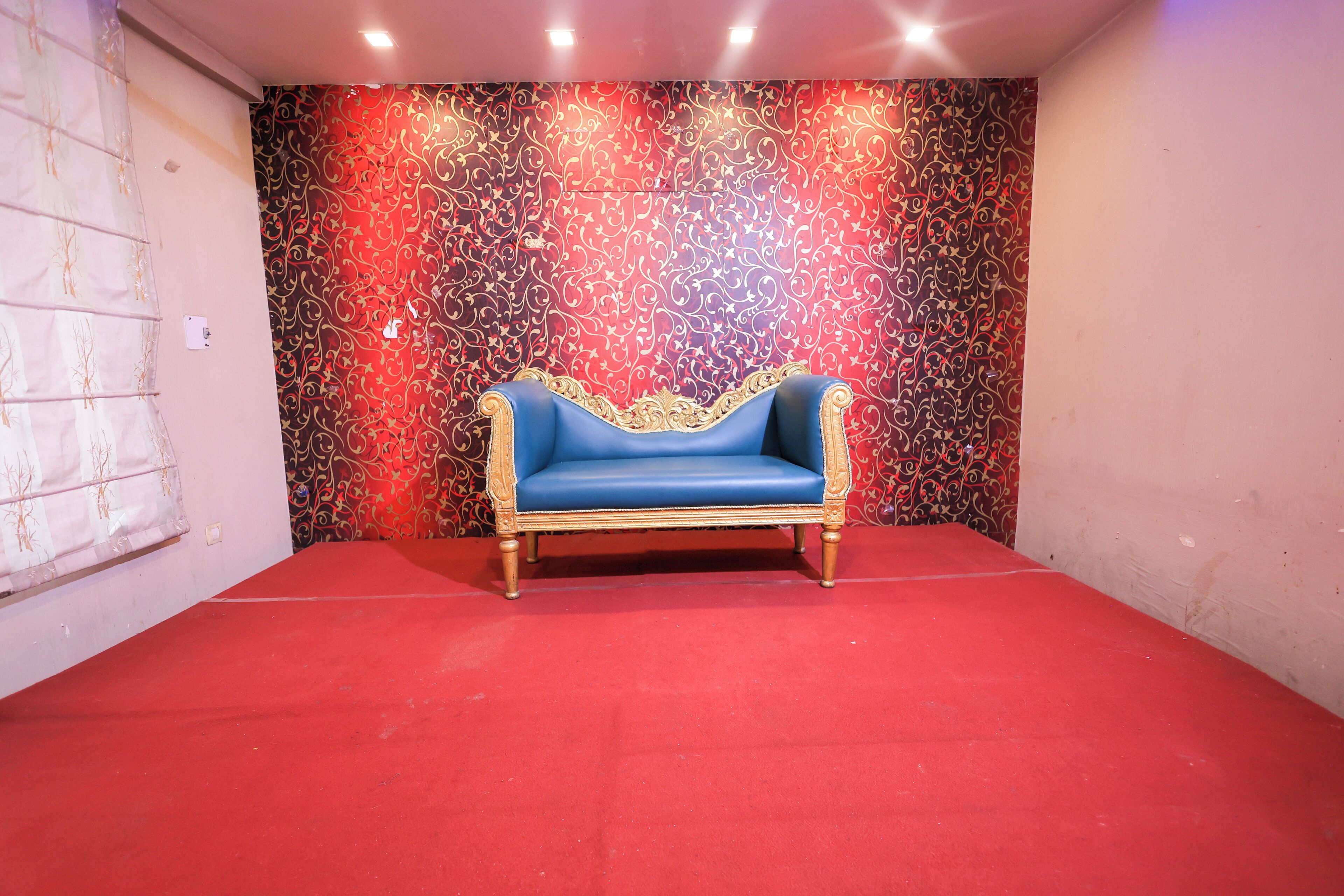 A room with a red carpet, a blue sofa with gold trim, and a patterned wall.