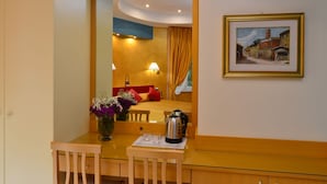 Habitación de hotel con cama, escritorio con hervidor, florero con flores y un cuadro en la pared.