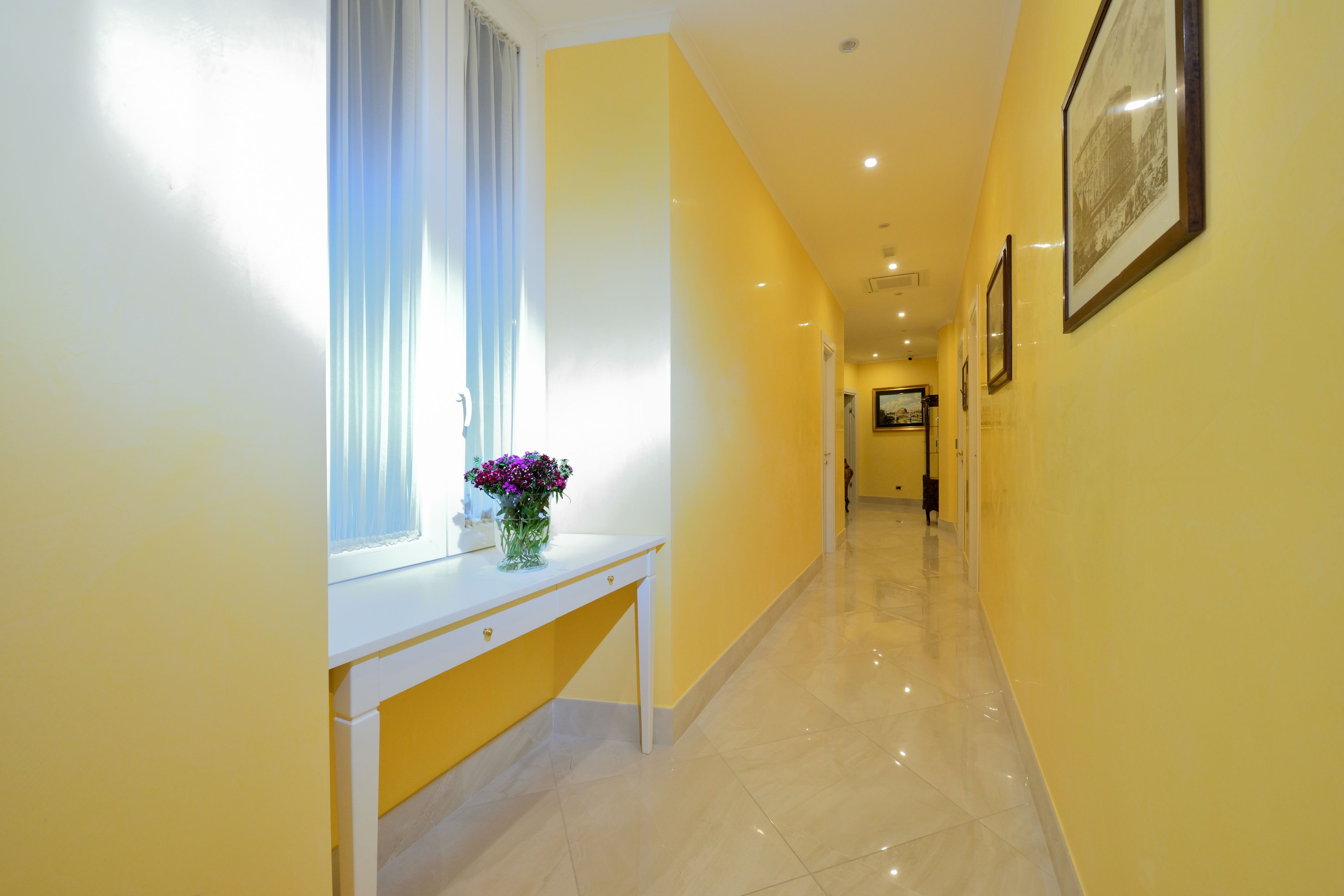 A hallway with a white console table and a vase of flowers, leading to a door at the end.