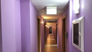 Un pasillo largo y estrecho con paredes moradas y piso de baldosas, que conduce a una puerta verde al final.