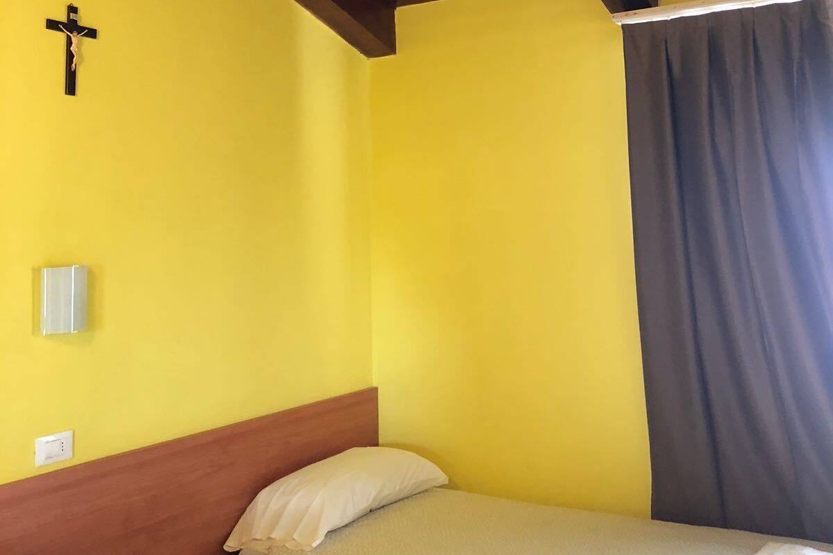 Una habitación con dos camas, vigas de madera en el techo, una cruz en la pared y una ventana con cortina.