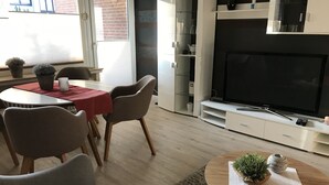 Moderni olohuone, jossa on takka, ruokailutila punaisella pöytäliinalla sekä viihtyisä oleskelualue pyöreän sohvapöydän ympärillä.
