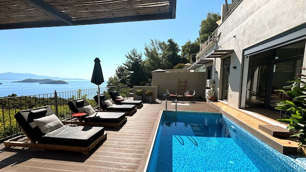 A poolside area with lounge chairs, a small table, and a view of the sea. - 3 Br 2 Bth Superior Villa  Cassiope with , Private Pool And Stunning Sea Views (Achladies)