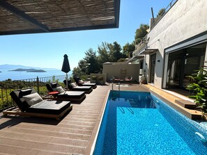 A poolside area with lounge chairs, a small table, and a view of the sea. - 3 Br 2 Bth Superior Villa  Cassiope with , Private Pool And Stunning Sea Views (Achladies)