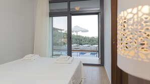 A hotel room with a bed, a balcony with a pool, and a view of trees and buildings. - 3 Br 2 Bth Superior Villa  Cassiope with , Private Pool And Stunning Sea Views (Achladies)