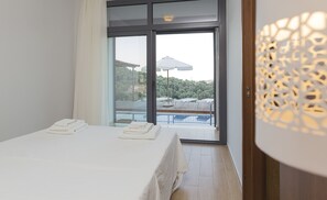 A hotel room with a bed, a balcony with a pool, and a view of trees and buildings.