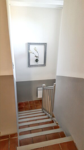 A narrow stairway with a metal railing, a white radiator, and a wall-mounted light fixture.