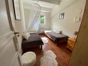 A small, well-lit bedroom with two single beds, a window, a dreamcatcher, and a wooden nightstand. - Homerez - Villa in Agde. (Agde)