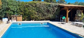 A swimming pool with a tiled deck, surrounded by a wooden pergola and a hedge. - Homerez - Villa in Agde. (Agde)