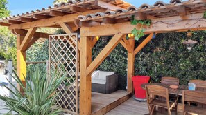A wooden pergola with a tiled roof, a wicker sofa, and a dining table with chairs. - Homerez - Villa in Agde. (Agde)