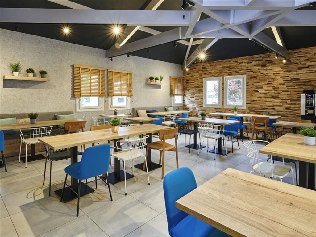 A modern cafe with multiple seating areas, including tables and chairs, and a rustic wooden wall.