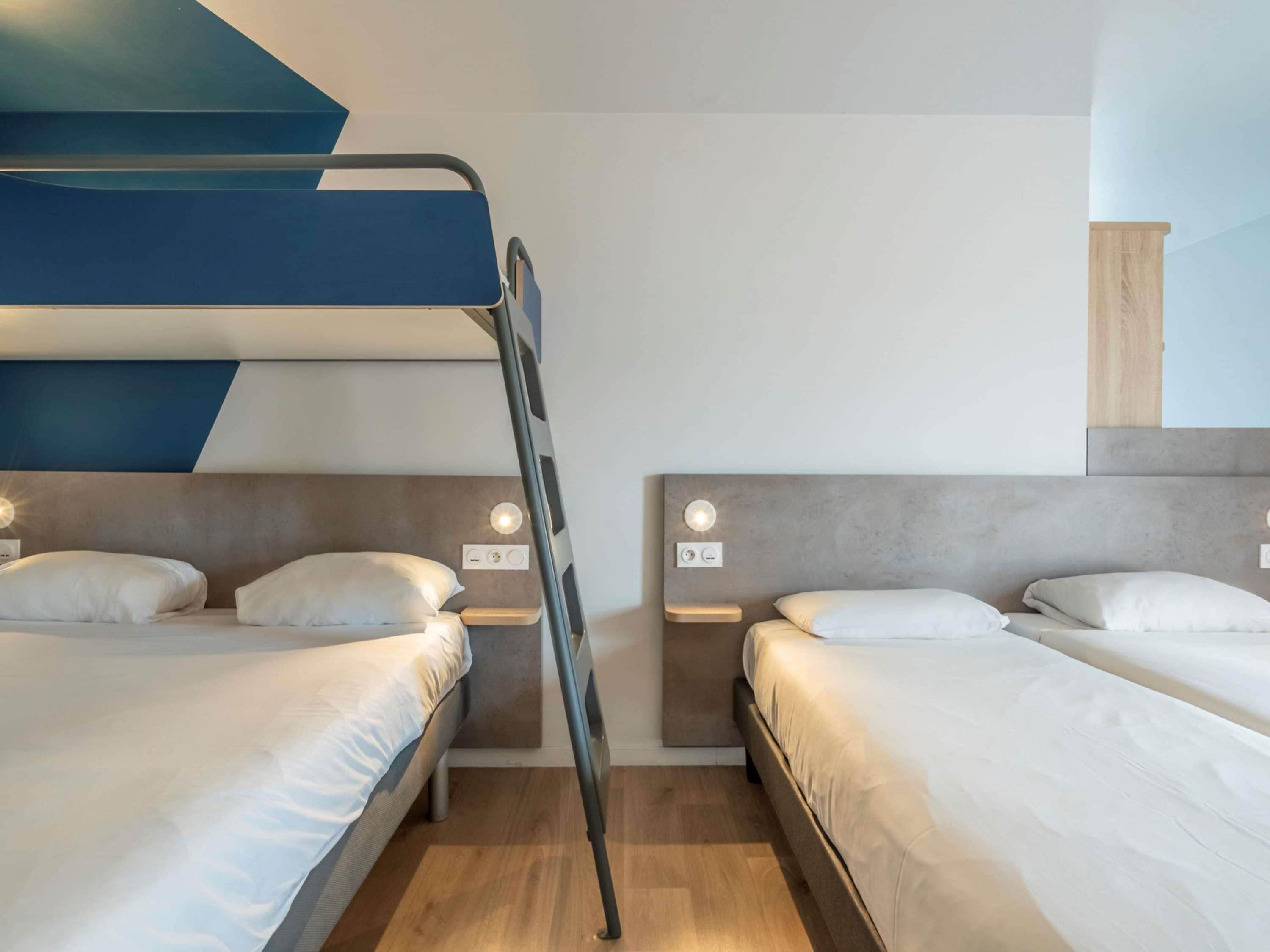 A hotel room with bunk beds, a bedside table, and a wall-mounted light fixture.