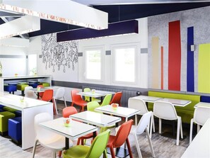 Un comedor moderno con sillas y mesas coloridas, un pared con diseño y ventanas grandes.