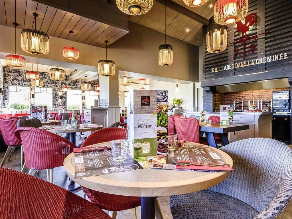 A restaurant interior with round tables, red chairs, and hanging pendant lights.
