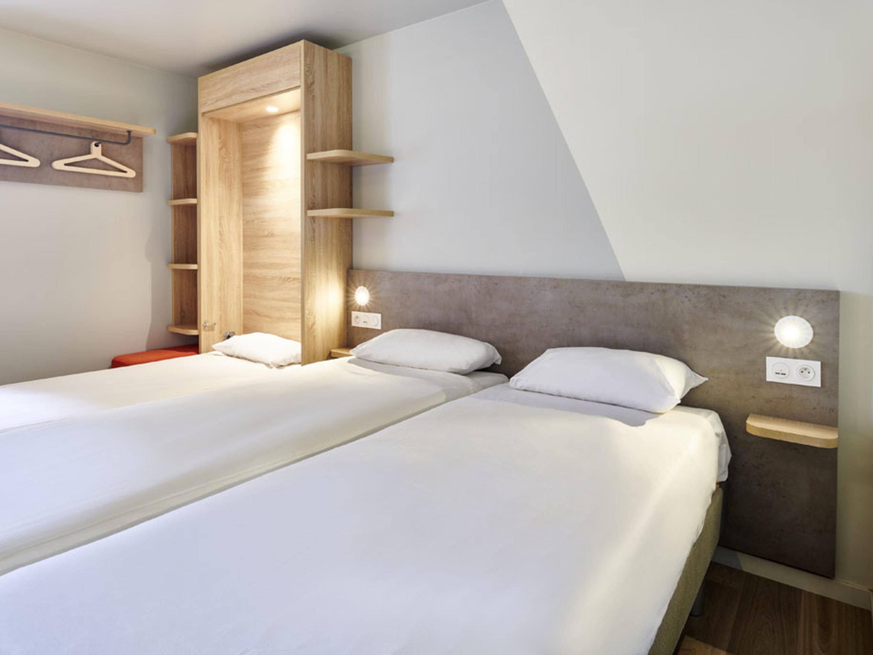 Una habitación de hotel moderna con dos camas, un armario de madera e iluminación empotrada.