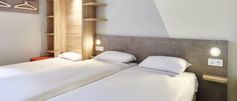 Una habitación de hotel moderna con dos camas, un armario de madera e iluminación empotrada.