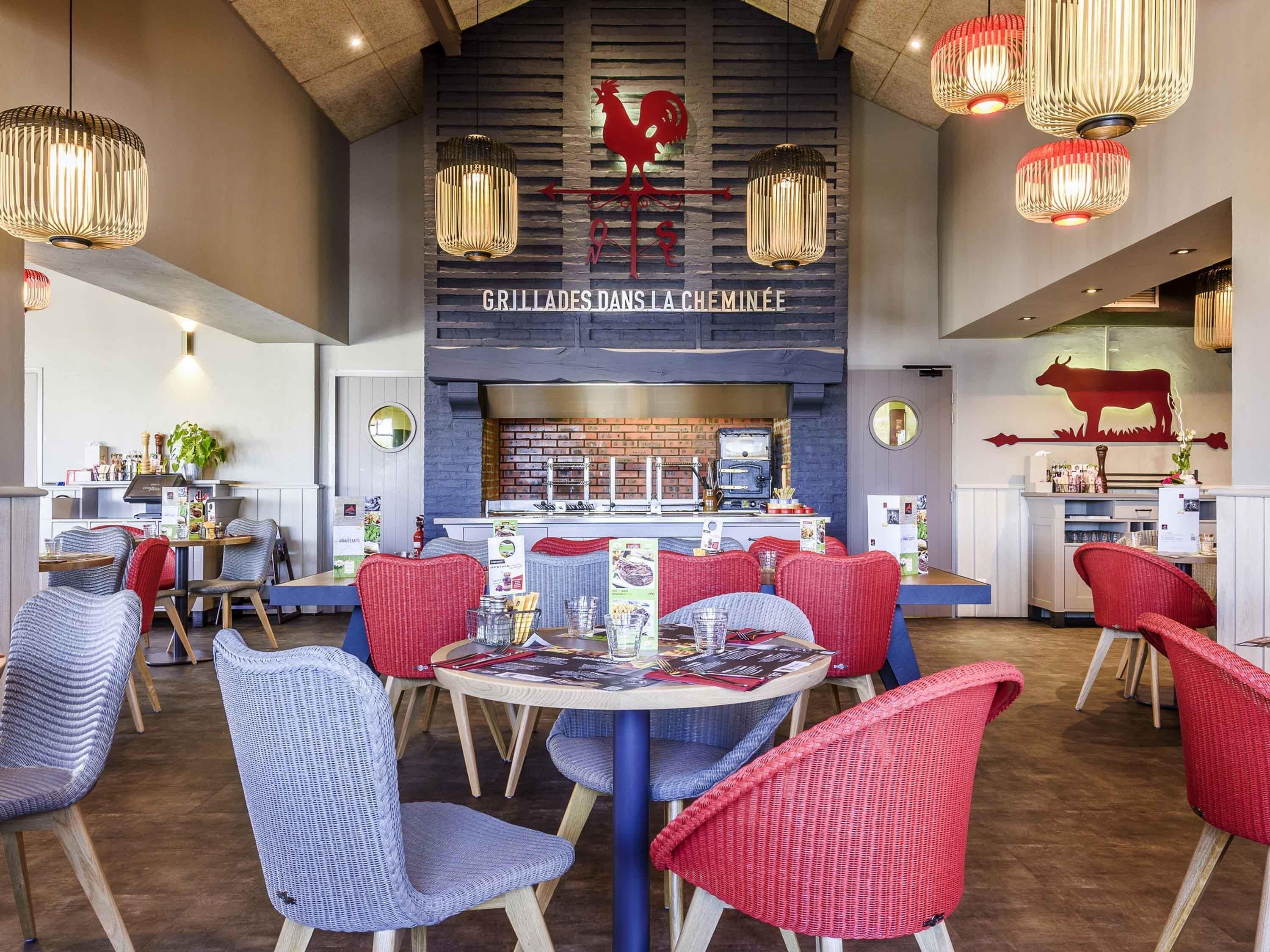 A restaurant interior with a bar area, red and blue wicker chairs, and hanging pendant lights.