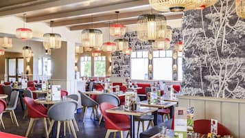 A restaurant interior with multiple dining tables, chairs, and hanging pendant lights.