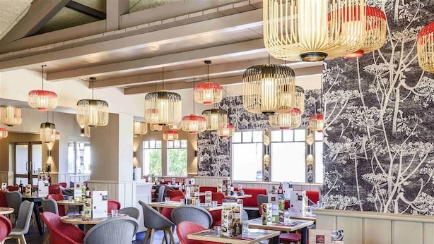 Un restaurant doté de nombreuses tables et chaises, de luminaires suspendus et d’une fresque murale.