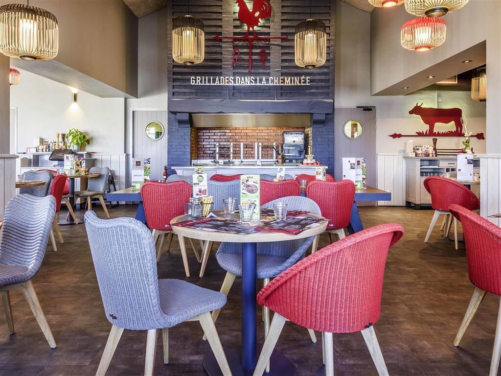 A restaurant with a central bar area, red and blue chairs, and hanging light fixtures.
