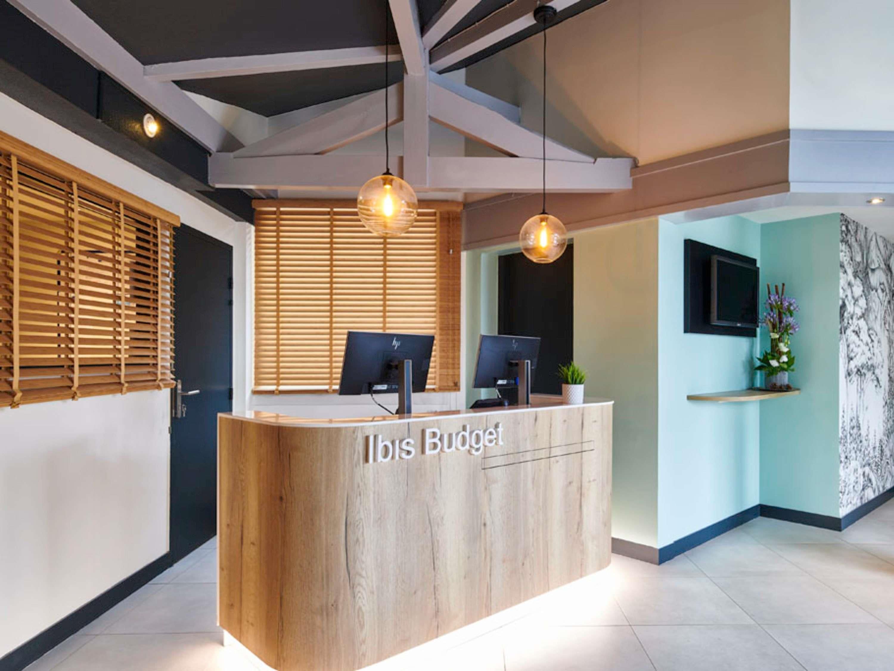 A reception desk with a wooden finish, two computer monitors, and a plant on a shelf.