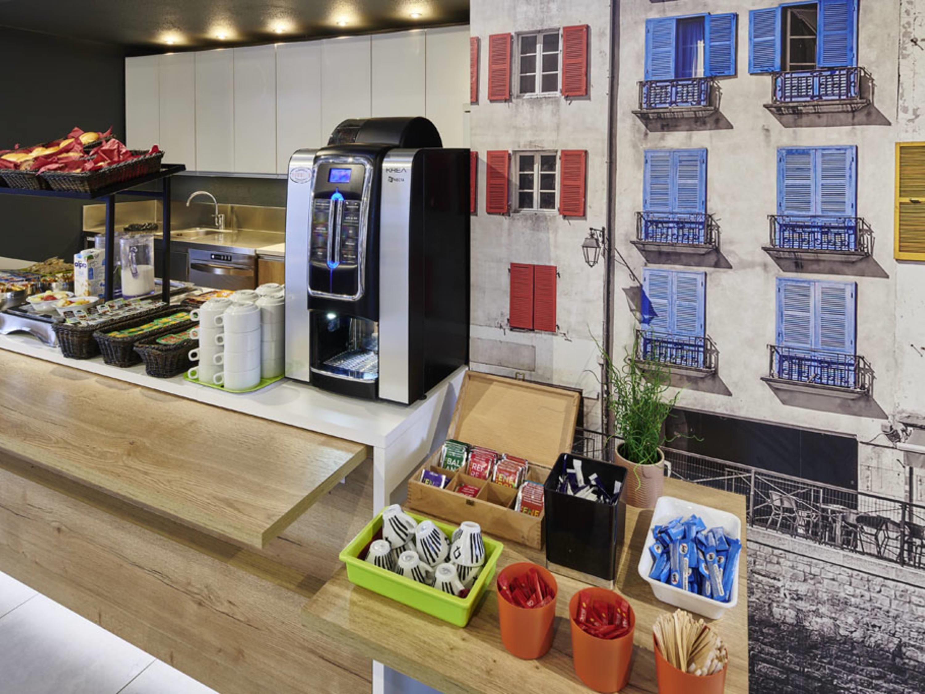 A breakfast bar with a coffee machine, food containers, and a wall with a mural of balconies.