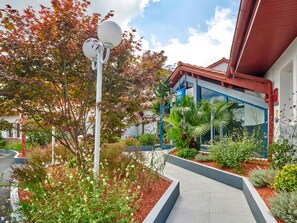 A modern building with a red roof, surrounded by a landscaped garden with various plants and flowers. - ibis Budget Bayonne (Bayonne)
