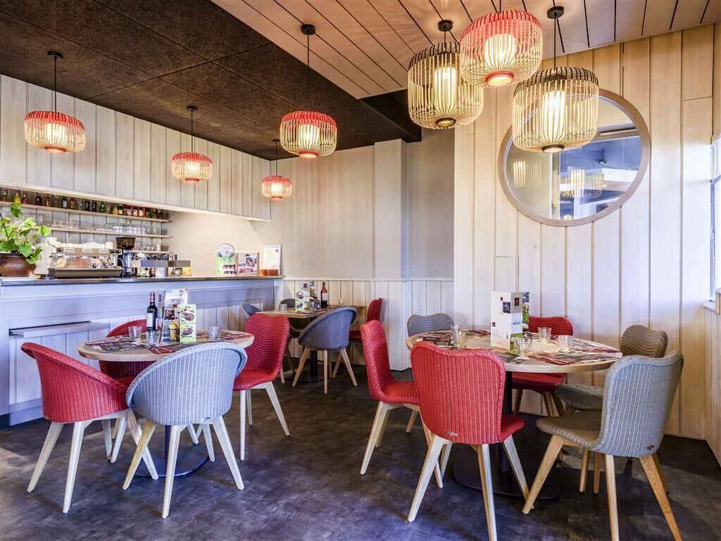 A restaurant with a bar area, red and grey chairs, and hanging red and beige pendant lights.