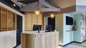 Un comptoir d’accueil équipé de deux écrans d’ordinateur, de stores en bois et d’un téléviseur fixé au mur.